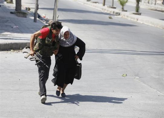 A Free Syrian Army fighter helps a woman to run across a street during clashes in Aleppo